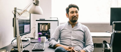 Person at desk with computer setup and coffee mug, face obscured.