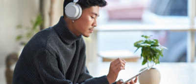 Seseorang mengenakan headphone dan menggunakan tablet.