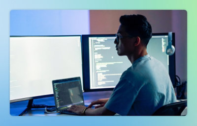 A Man sitting at a desk with a laptop and a monitor.