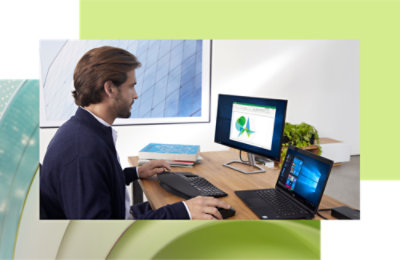 Ein Mann, der an einem Computer und Laptop an einem modernen Bürotisch arbeitet und Daten auf einem Bildschirm mit grafischen Diagrammen analysiert.