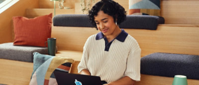  Person using a laptop while seated in a modern workspace with tiered seating and cushions.