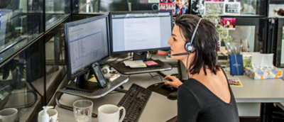 En kvinne med headset som sitter ved et skrivebord med flere dataskjermer.