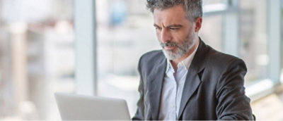 Un uomo con i capelli grigi e la barba lavora su un computer portatile in un ufficio luminoso e moderno.