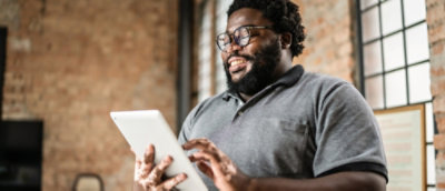 Un homme barbu souriant qui utilise une tablette dans un espace de travail de type loft.