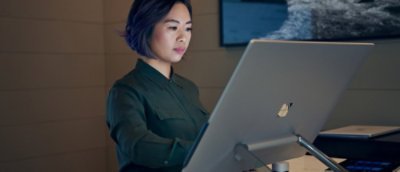 A laptop on a stand with a person in a green shirt visible in the background.