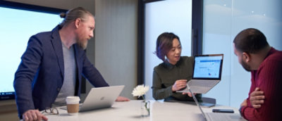 Trois professionnels discutant sur un ordinateur portable dans un environnement de bureau moderne.