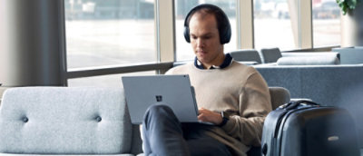 A man in a collared shirt working on a laptop in a modern office environment.