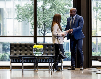 Ein Mann und eine Frau, die sich in einer modernen Bürolobby unterhalten und dabei in der Nähe eines schwarzen Sofas und gelber Blumen stehen