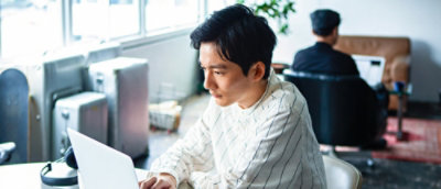 A man wearing white t short working on a laptop.