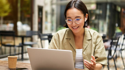 Uma pessoa usando óculos e fones de ouvido está sentada à mesa usando um laptop.