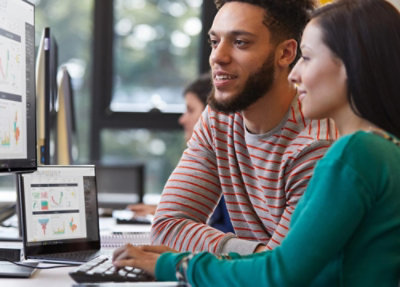 Deux collègues assis à un bureau, examinant des graphiques et des visualisations de données sur un ordinateur portable et un moniteur externe dans un espace de travail moderne.