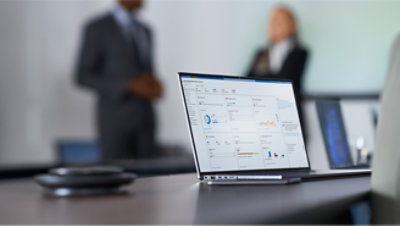 A laptop is on a desk with people in the background.