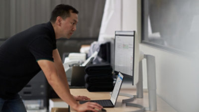 Une personne penchée au-dessus d’un bureau et utilisant un ordinateur portable connecté à un écran