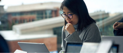 Uma mulher de óculos lê atentamente no laptop em um ambiente de escritório moderno.