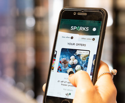 En hånd, der holder en smartphone, der viser Sparks-appen med forskellige tilbud, der er synlige på skærmen.