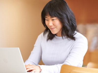 검은 머리의 젊은 여성이 연한 터틀넥 스웨터를 입고 노트북 작업에 집중하고 있습니다.