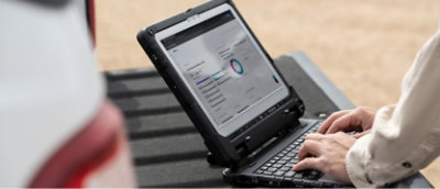 Person som skriver på en robust bærbar PC plassert bak i et kjøretøy, med en skjerm som viser et dashbord med diagrammer og data.
