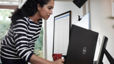 Personne se tenant à un bureau équipé de plusieurs écrans et d’un ordinateur portable