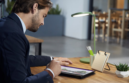 Photograph of a person seated at a desk working on a tablet with a stylus