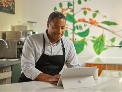 Önlüklü bir adam Microsoft Surface tablet kullanıyor.
