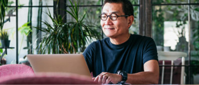 眼鏡をかけて黒いシャツを着た人が、植物のあるテーブルに向かって座り、ノート PC で作業しています。