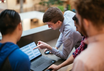 Fotografía de un grupo de personas delante de un mostrador mirando la pantalla de un portátil con la función de accesibilidad de la lupa de Windows que hace que sea más fácil leer textos.