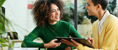 A woman in a green shirt holding a tablet and smiling.