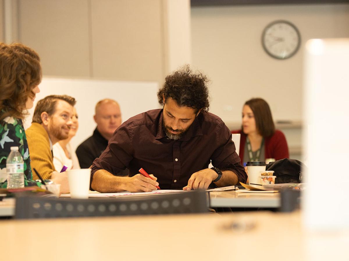 man writing with focus while surrounded by others in a classroom
