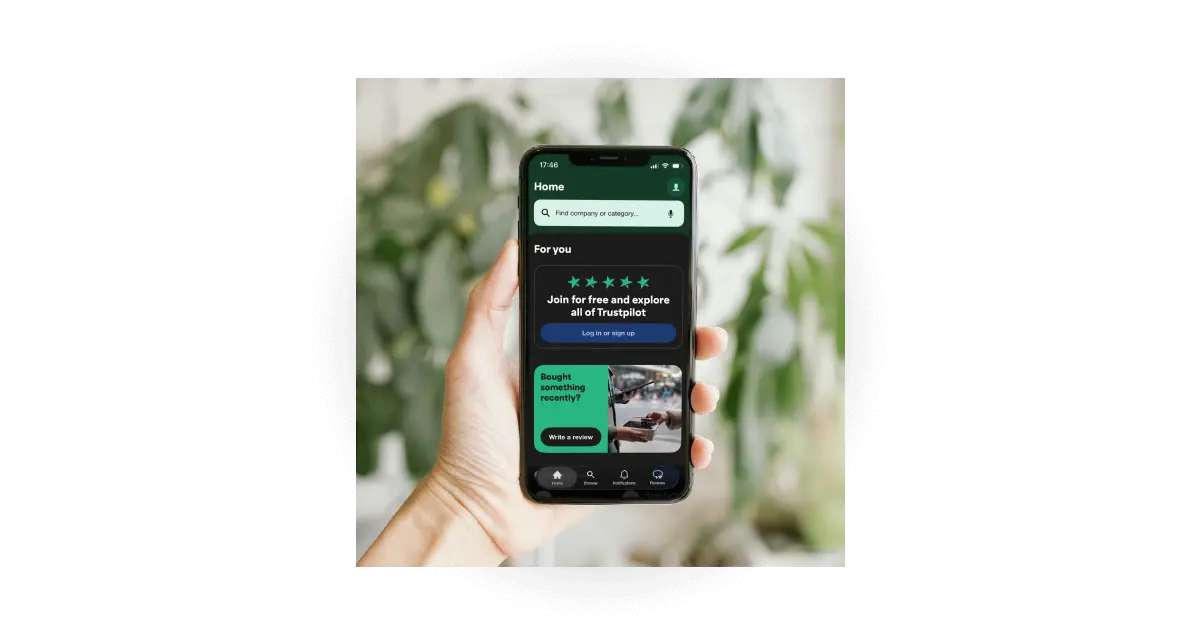 A hand holding a smartphone displaying the Trustpilot app homepage with a prompt to join for free and review recent purchases.