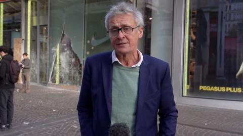 Hugh Schofield holding a microphone speaking on a Paris street.