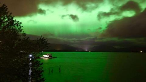 Deep green aurora over Loch Lomond with a boat in the foreground.