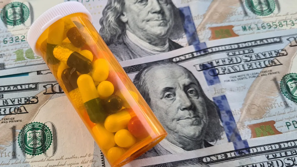 A bottle of pills lays on top of a sheet of $100 bills.