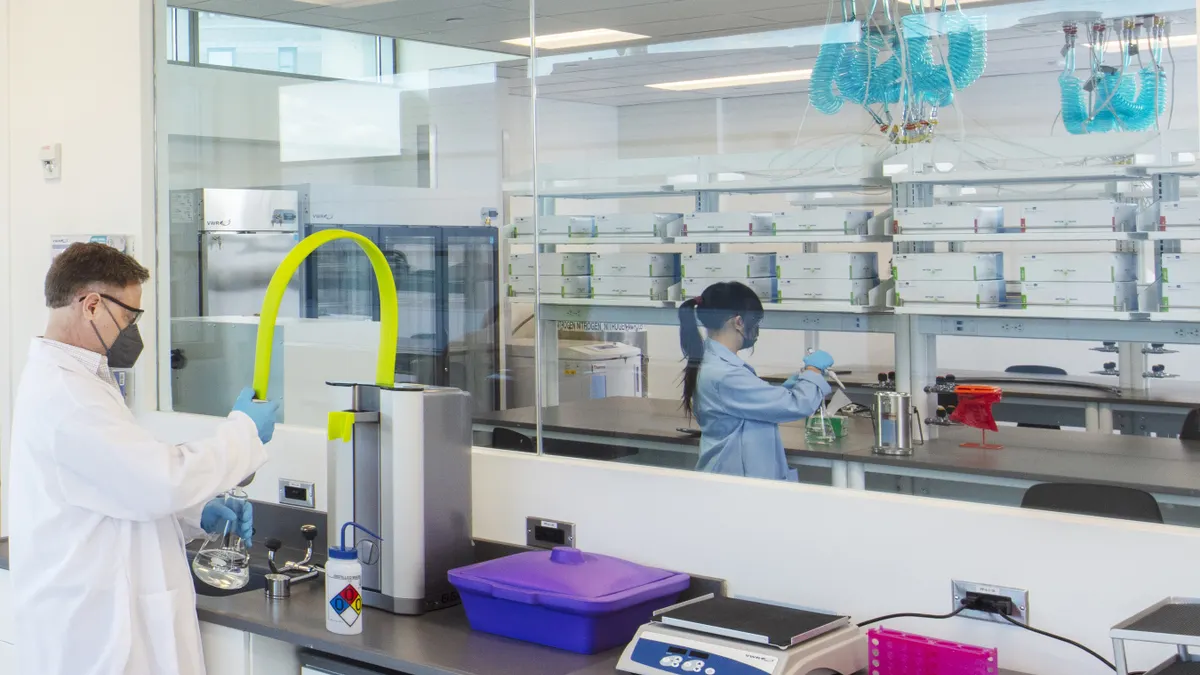 Two people in white coats work at a laboratory benchtop.