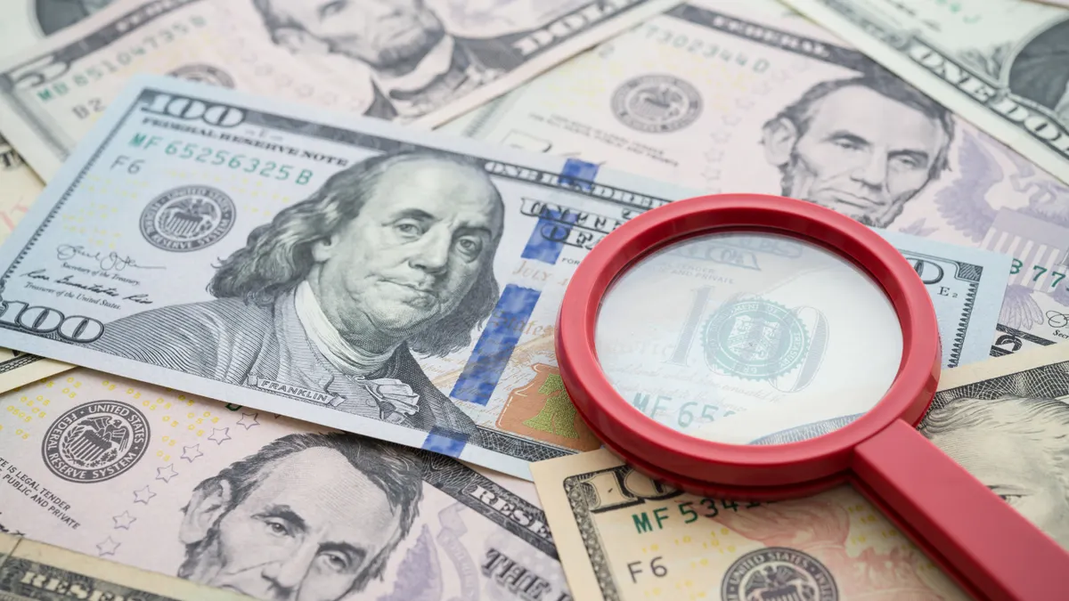A red magnifying glass sits on top of cash.