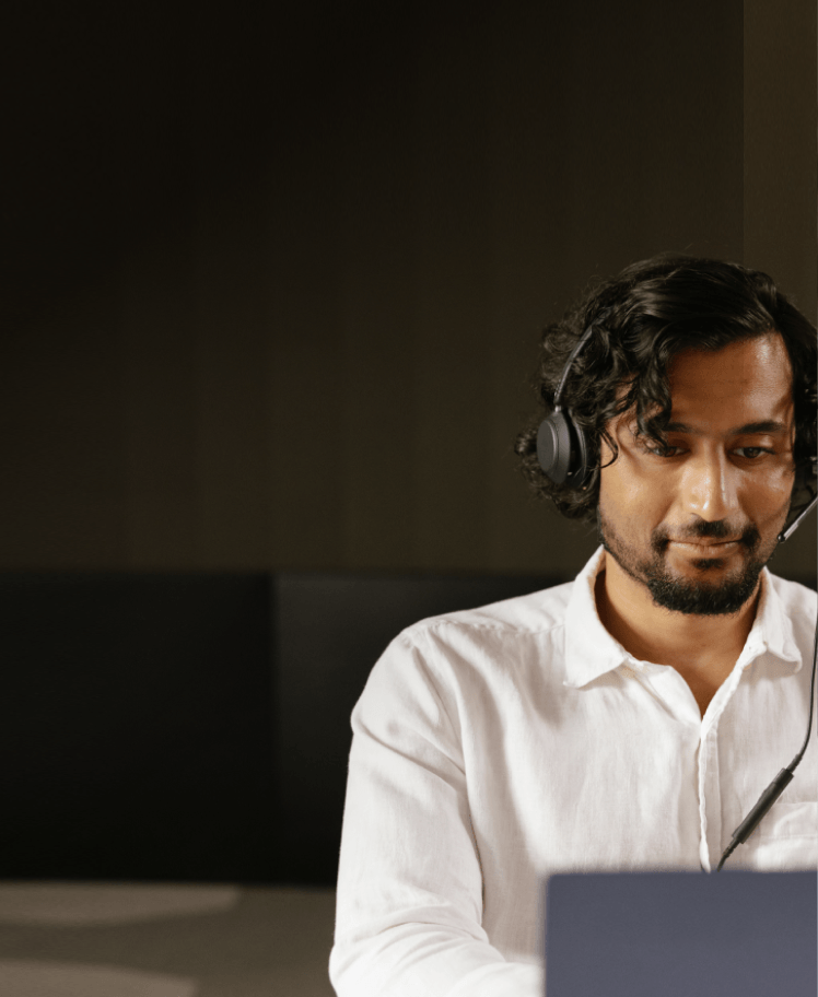 A man wearing a headset works on a laptop in a dimly lit office.