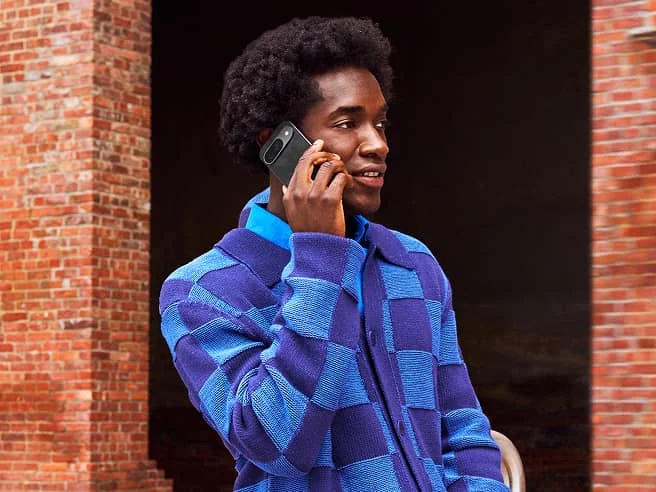 An individual leaning against a brick wall on the phone using a Google Pixel device.