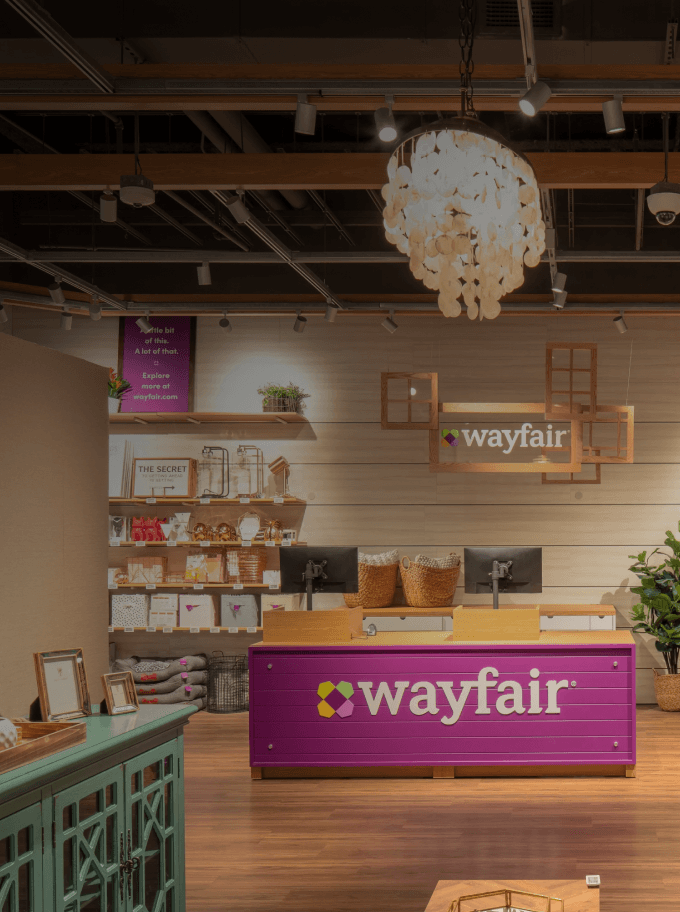 Wayfair retail store checkout counter with Wayfair branding and display shelves stocked with merchandise.