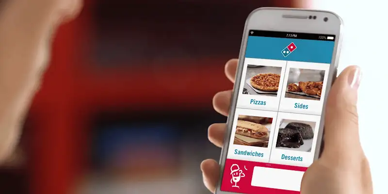 Person using Domino's app on a smartphone to order pizza, sides, sandwiches, and desserts.