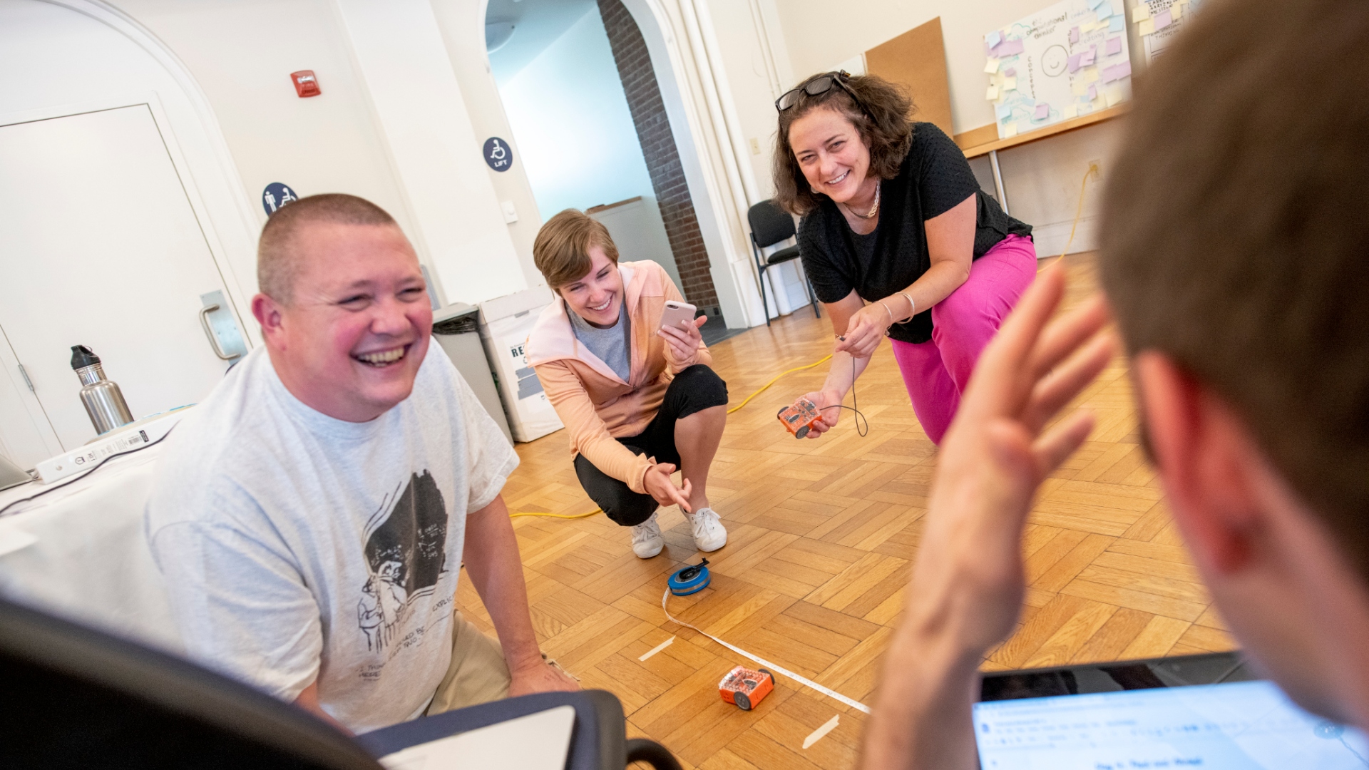 four people crouching on the floor smiling and using measuring tape