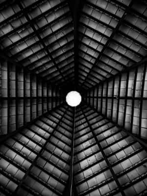 A black and white photo of a symmetrical industrial ceiling with a central light bulb. — iPad Air 13 Wallpaper