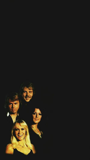 Four smiling musicians in vintage 1970s style posing in a dark studio with golden lighting. — Abba Wallpaper