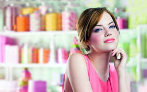 Mujer con blusa rosa mirando pensativamente en una tienda de belleza con productos coloridos detrás de ella. — Actriz Fondos de pantalla