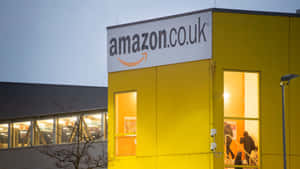 Extérieur d'entrepôt Amazon UK au crépuscule avec fenêtres illuminées et personnes entrant. — Amazon Fonds d'écran