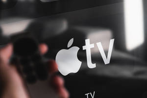 Mano sosteniendo control remoto apuntando a pantalla de Apple TV con logotipo enfocado. — Logo Fondos de pantalla