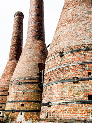 Weathered brick industrial chimneys with black metal bands against a bright sky. — Authentic Wallpaper