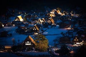Snowy mountain village at night with glowing thatched roofs and visitors. — Authentic Wallpaper