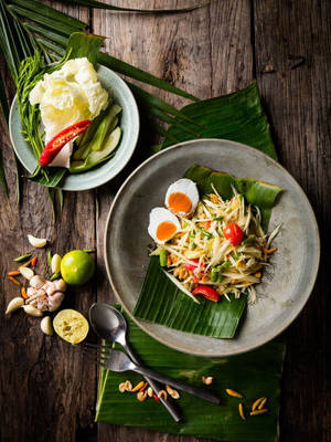 Thai papaya salad with boiled eggs and lime on banana leaves on wooden table — Authentic Wallpaper