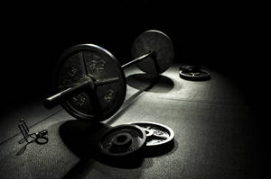 A barbell and weights lit by a spotlight on a gym floor. — Barbell Wallpaper