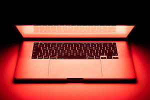 Un ordinateur portable rouge lumineux sur une surface sombre avec un éclairage ambiant. — MacBook Fonds d'écran