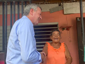 A man and elderly woman smiling while shaking hands outside a pink building. — Local Wallpaper